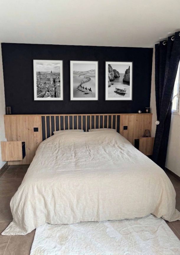 Aménagement de bibliothèque sur mesure sous pente avec étagères ouvertes et rangements fermés, intégrée dans un espace chaleureux avec un sol en parquet clair, un tapis graphique noir et blanc, et des éléments décoratifs comme une guitare et un ampli.