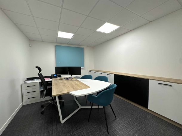 Bureau de direction moderne aménagé sur mesure, avec une grande table en bois et blanc, des fauteuils bleus, des rangements bas en bois clair, blanc et noir, et un store bleu apportant une touche de couleur.